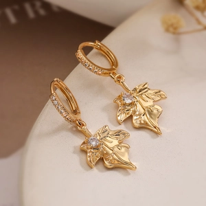 Gold maple leaf drop earrings with white zircon crystals on a minimalist stone surface