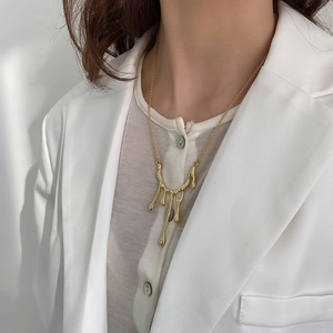 Close-up of golden liquid lava pendant necklace on model with white blazer