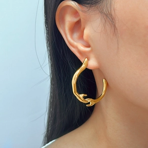 Gros plan de boucles d'oreilles créoles dorées abstraites sur mannequin, fond bleu