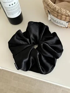 Detail shot of large black satin hair scrunchie with fashion label on white surface