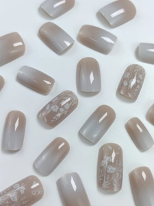 Detail of white gradient press-on nails with delicate hand-painted floral and leaf patterns