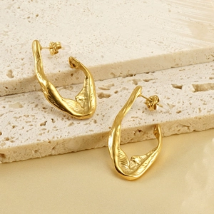Irregular wave gold earrings on white stone pedestals with a luxury silk background