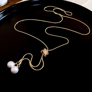Détail d'un collier chaîne serpent dorée avec deux grandes perles et une boule sertie