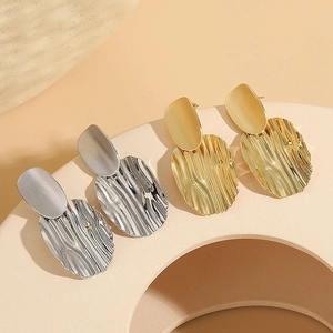 Exaggerated irregular wrinkled gold and silver drop earrings on a stone base