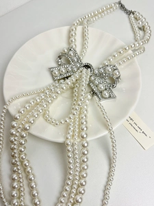 Detailed view of multi-layer pearl necklace with a silver crystal bow on a ceramic plate