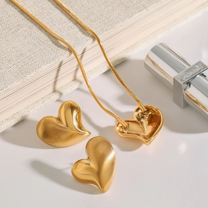Detailed view of matte gold heart necklace and earring set on a minimalist background