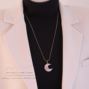 Dettaglio della collana a mezza luna con pietra rosa su maglione nero e blazer beige