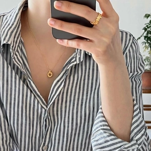 Close-up of golden round rope pendant necklace and hollow textured ring on a model