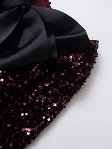 Close-up of sparkling burgundy sequins fabric with a large black grosgrain bow accent