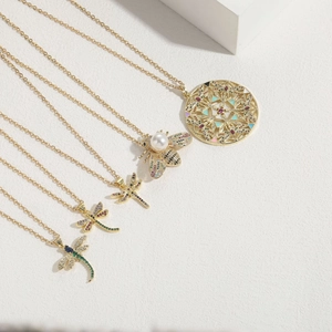 Dettaglio di pendenti ape e libellula con zirconi colorati e perle su catene d'oro