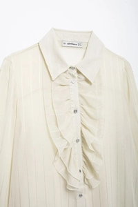 Detail of ruffle collar and button-up front on a cream long-sleeved women blouse
