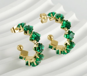 Macro view of gold-plated C-shaped earrings with square-cut emerald green zircons