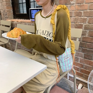 Detail of checkered crossbody bag with yellow ruffled strap and green patchwork shirt