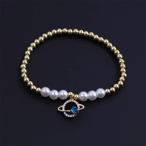 Saturn charm bracelet with gold beads, white pearls and blue star zircon on black surface