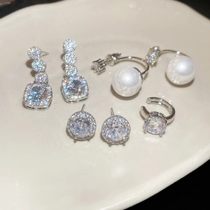 Close-up of sparkling cubic zirconia geometric earrings and pearls on ceramic tray