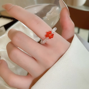 Detail of a handmade elastic beaded ring featuring a red flower and clear acrylic beads