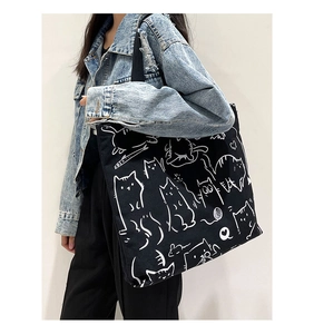 Detail of black canvas tote bag with white cat illustration worn by a female model
