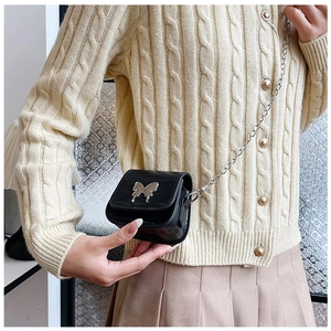 Close-up of a mini black saddle bag with silver butterfly buckle and chain strap