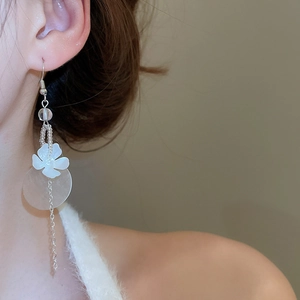 Detail of elegant long tassel earrings with white flower petals and geometric shell disks