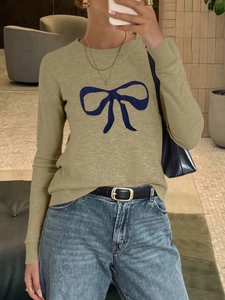 Detail of khaki knit sweater showing blue bow design and ribbed cuffs in lifestyle setting