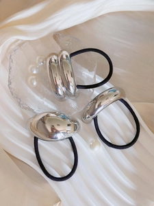 Close-up of three minimalist silver geometric metal hair ties on white silk fabric