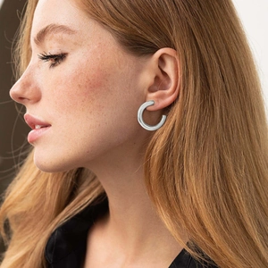 Close-up of thick silver-tone C-shaped hoop earring on a model's ear for style