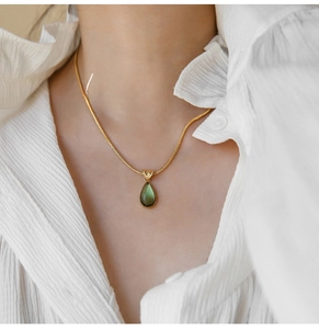 Detail of vintage teardrop necklace with green gemstone on gold snake chain worn by model