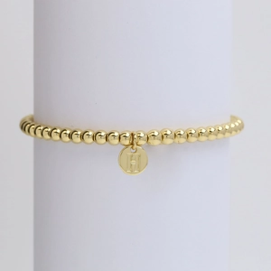 Detailed macro view of gold beaded bracelet featuring a round letter H alphabet pendant