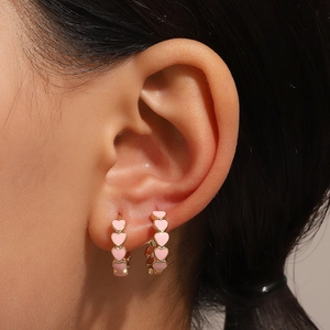 Close-up of heart-shaped gold hoops with pink enamel finish worn by a model