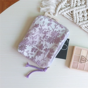 Détail de broderie florale sur pochette en coton crème avec fermeture éclair violette