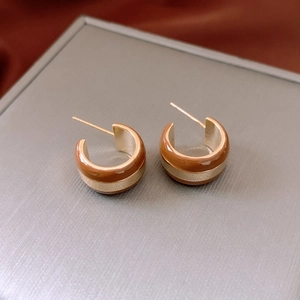 Detail of gold-plated striped C-shaped earrings with caramel enamel on a display box