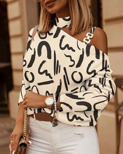 Detalle de blusa con hombro descubierto, cadena, hebilla dorada y estampado abstracto