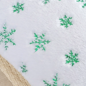 Macro shot of plush white fabric with green sequined snowflake embroidery on pillow cover