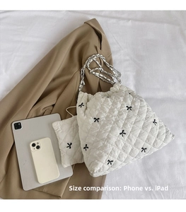 White quilted shoulder bag with black bows and silver chain strap shown beside an iPad