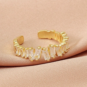 Adjustable gold open ring featuring a row of baguette-cut zircons on a pink fabric background
