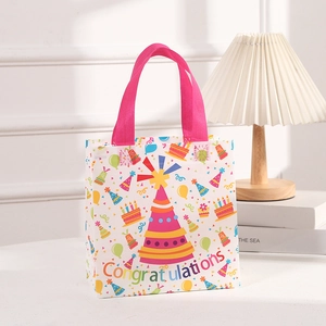 Colorful non-woven birthday gift bag with festive prints and pink handle on white desk
