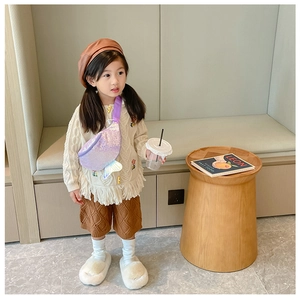 Kid model wearing a purple sequin mermaid tail bag over a beige knit cardigan sweater