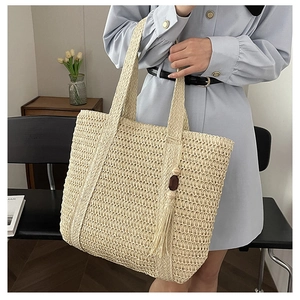 Detail of beige woven straw tote bag with elegant tassel and wooden bead charm