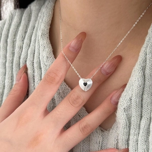 Detailed view of a silver heart necklace with black stone on a green knit sweater