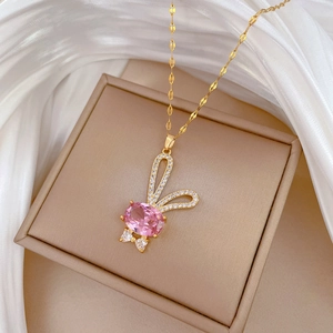 Collier lapin doré avec pierre rose et cristaux présenté sur un coffret à bijoux beige
