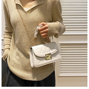 Detalle de bolso acolchado blanco con cadena dorada y asa plisada llevado por modelo