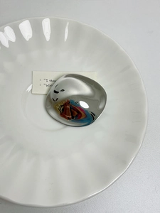 Close-up of irregular silver geometric brooch on a white porcelain plate with a fluid design