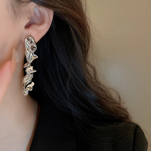 Close-up of silver irregular liquid metal earrings worn by a model in a natural side view