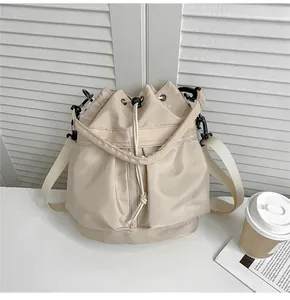 Detail of cream drawstring nylon bucket bag with dual front pockets and metal hooks