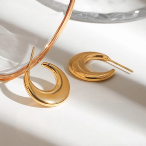 Close-up of polished golden C-shaped stainless steel earrings on a clean surface