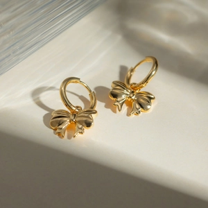 Polished 18k gold-plated stainless steel bow earrings on a sophisticated glass surface
