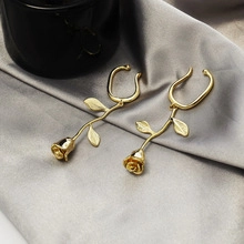 Detail of elegant gold rose-shaped long ear cuffs with leaves on grey silk fabric