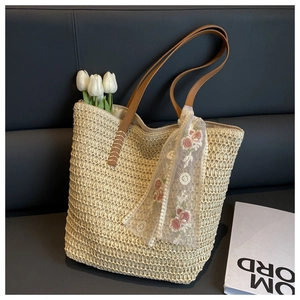 Detail view of woven straw bucket bag with brown leather handles and floral lace scarf