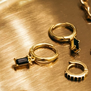 Macro view of gold hoop earrings with rectangular black gemstone and small zircon inlay