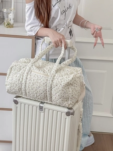Borsa da viaggio trapuntata a fiori con tracolla sopra una valigia bianca